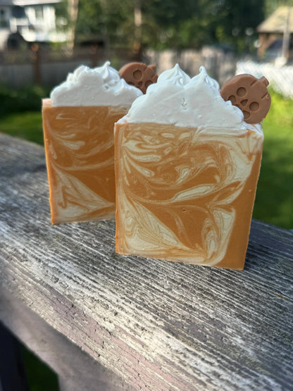 Two Square soap bar with swirls of cream, orange, and warm brown, sitting on a wooden railing..