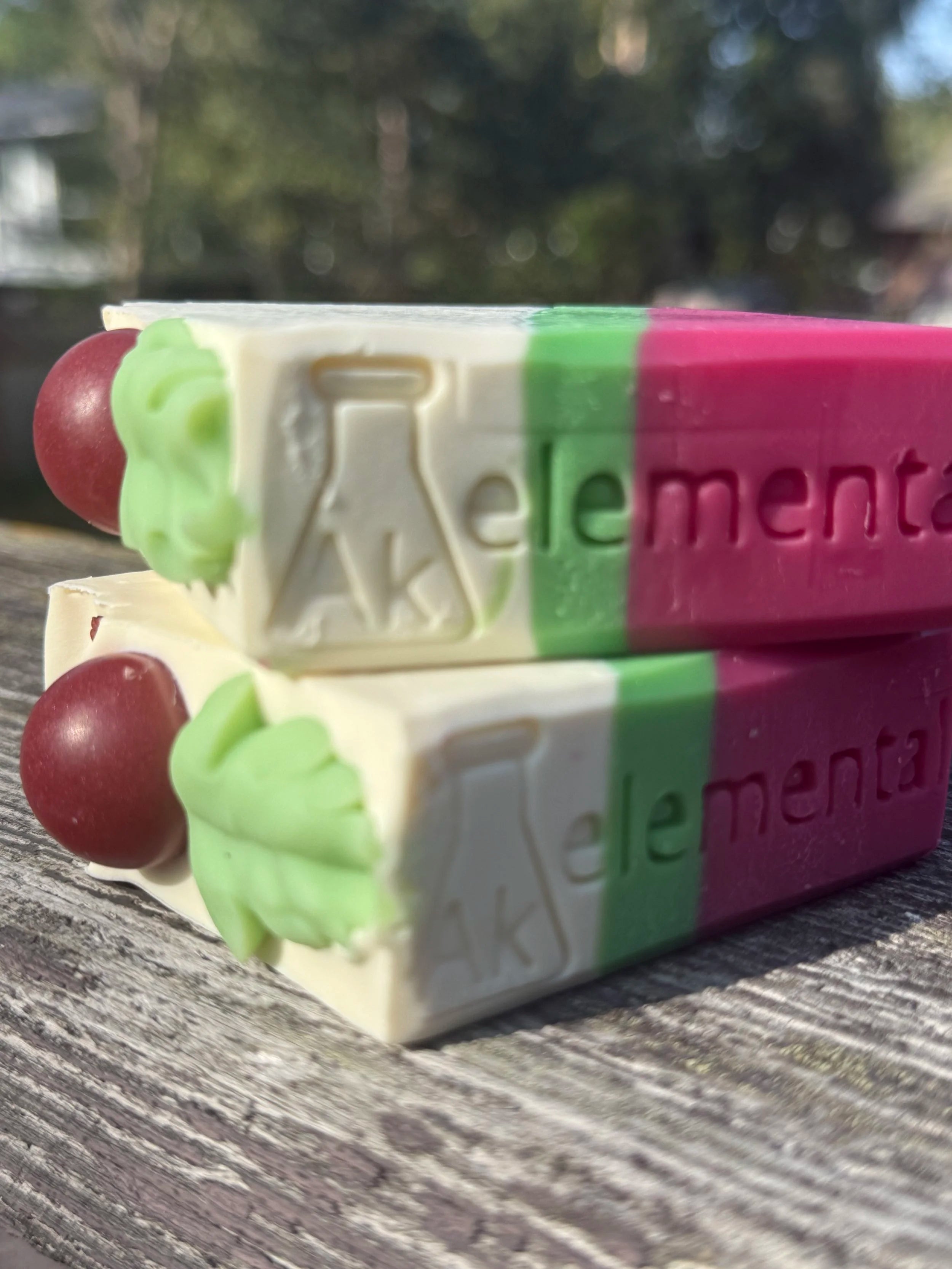 Side view of two Handcrafted Wild Cranberry soap bars with cream, evergreen green and cranberry red diagonal layers and festive round soap embeds on top.