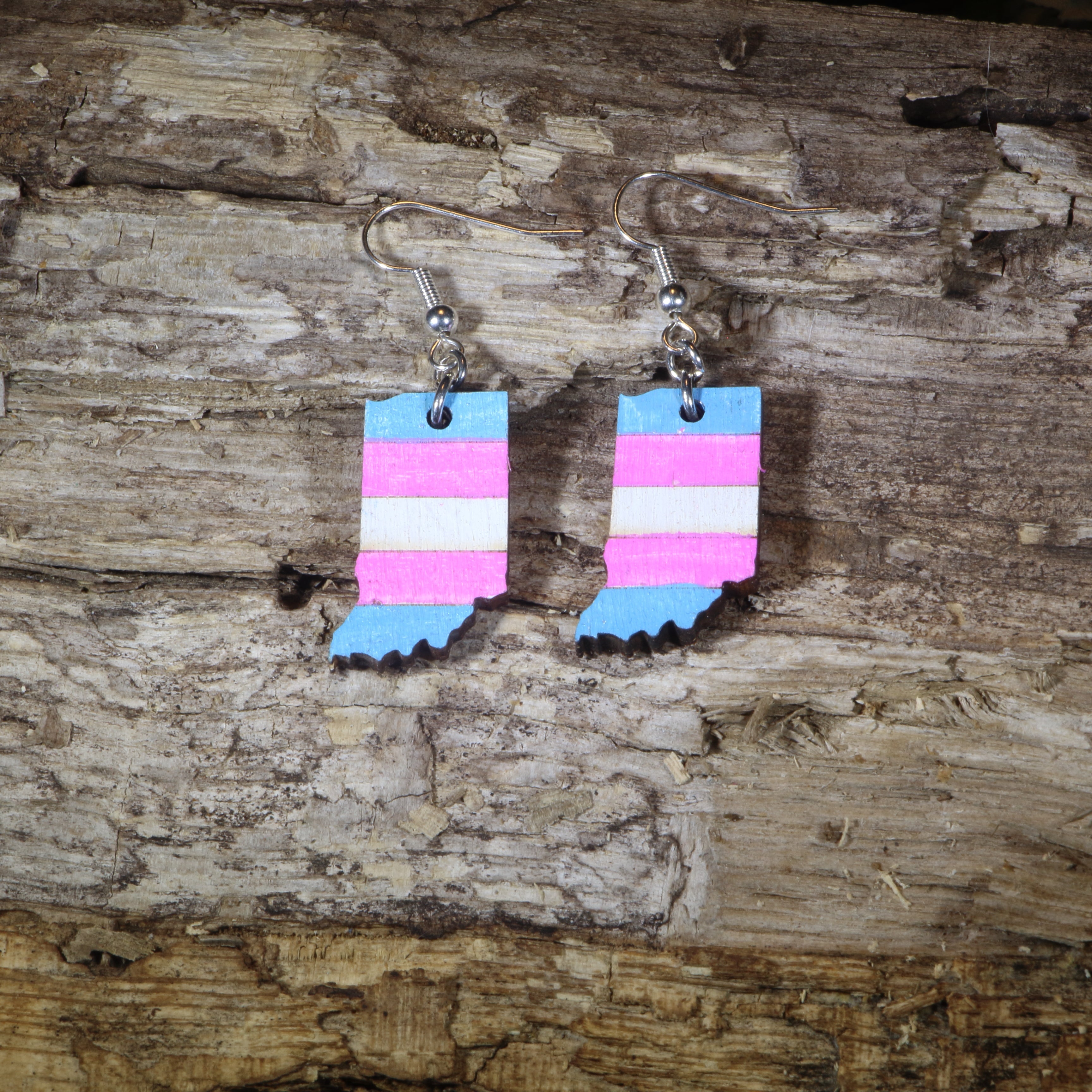 Hand-painted wooden Indiana transgender pride dangle earrings featuring the Indiana state silhouette with pink, blue, and white transgender pride stripes, hypoallergenic sterling silver hooks, and lightweight LGBTQ+ state pride jewelry by Cate&