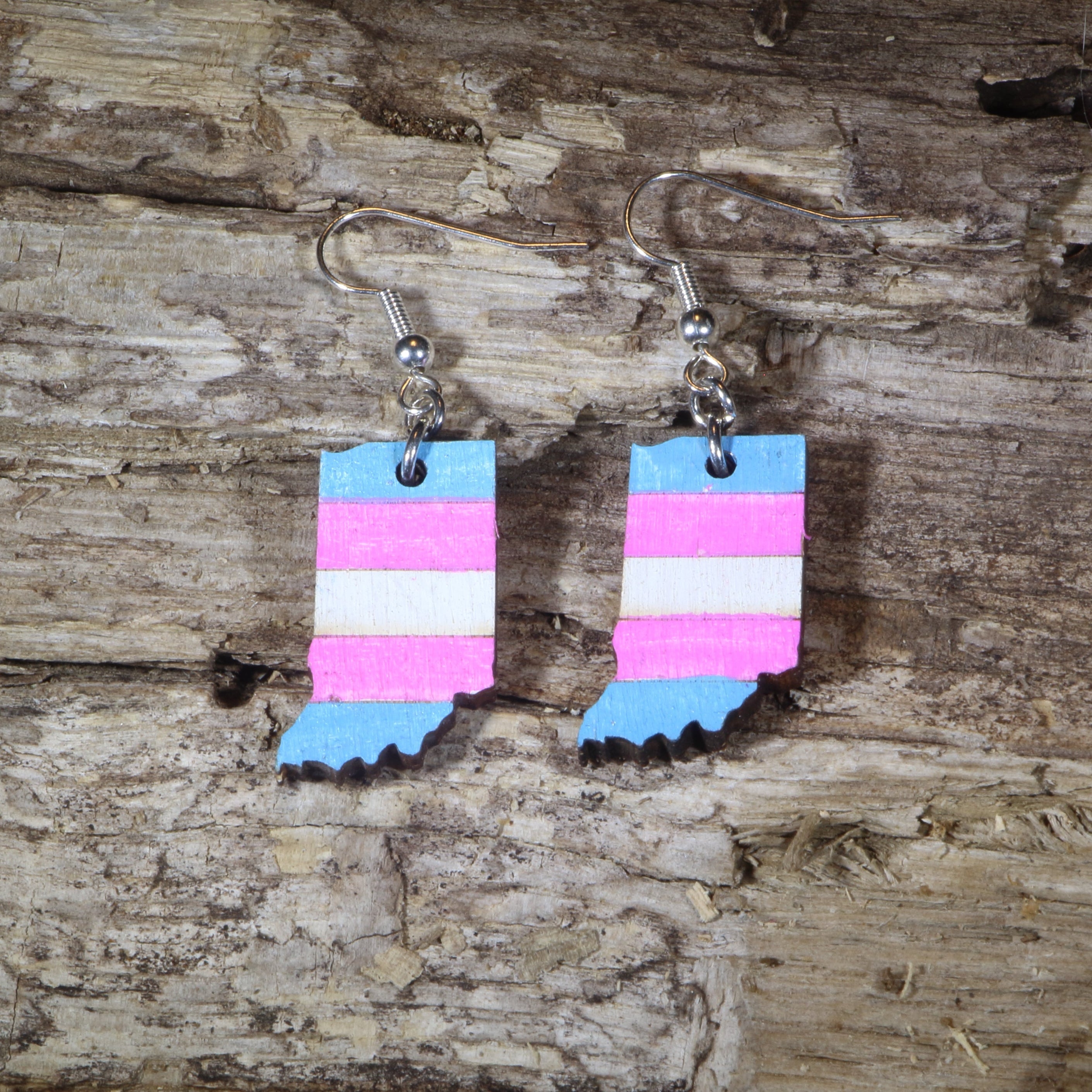 Hand-painted wooden Indiana transgender pride dangle earrings featuring the Indiana state silhouette with pink, blue, and white transgender pride stripes, hypoallergenic sterling silver hooks, and lightweight LGBTQ+ state pride jewelry by Cate&