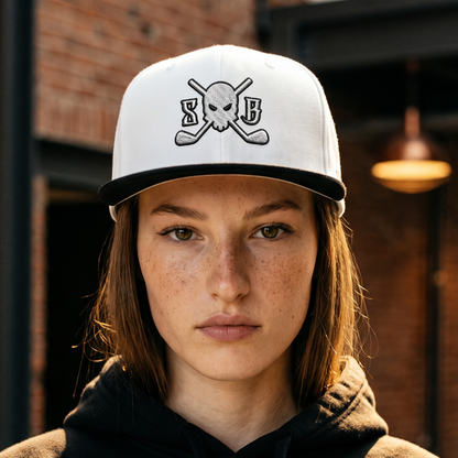 A person wearing a white baseball cap with a black brim and a black-and-white skull-and-crossbones graphic with the letters &