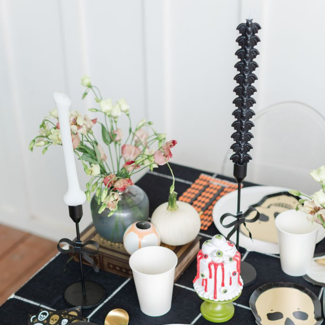 Black bat taper candle in a candlestick, styled Halloween table with florals and a skull plate.
