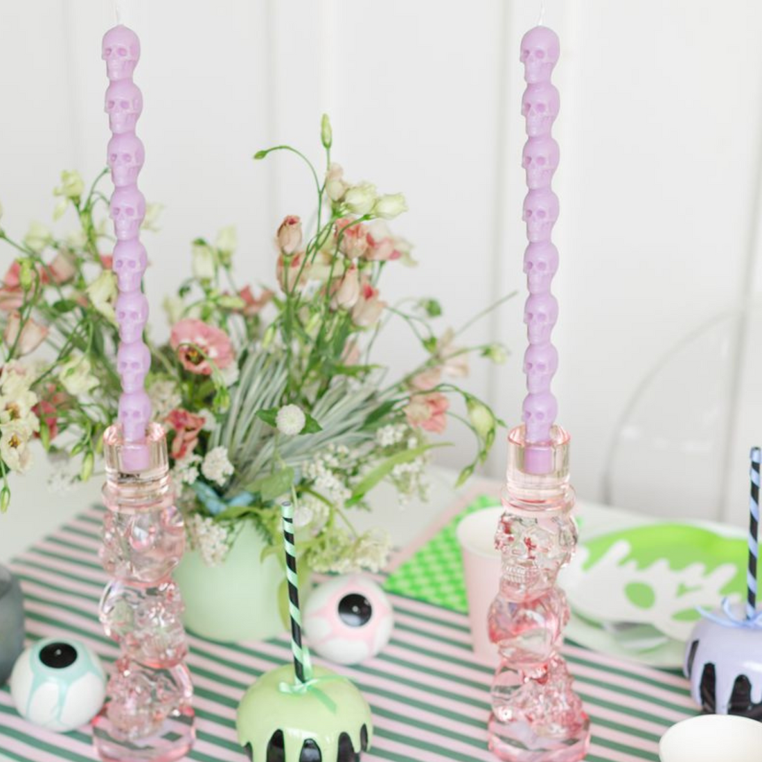 Light purple stacking-skull taper candles in pink glass holders, pastel table styling.