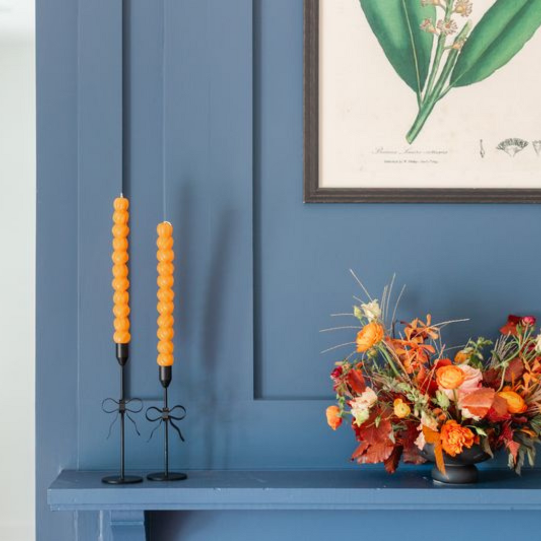 Orange stacking-pumpkin taper candles in black candlesticks, styled with autumn florals.