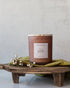 Joy candle in amber glass jar on dark wood surface, evoking floral and citrus notes – Fig & Grove