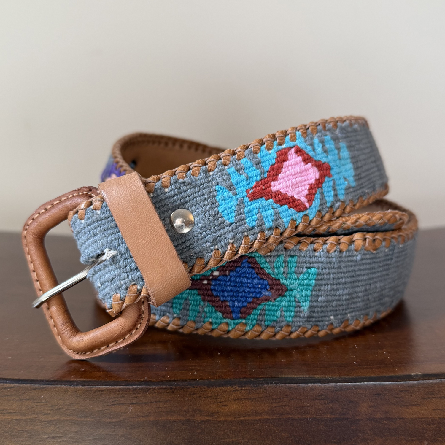 Decorative belt with floral pattern and brown leather buckle on a wooden surface
