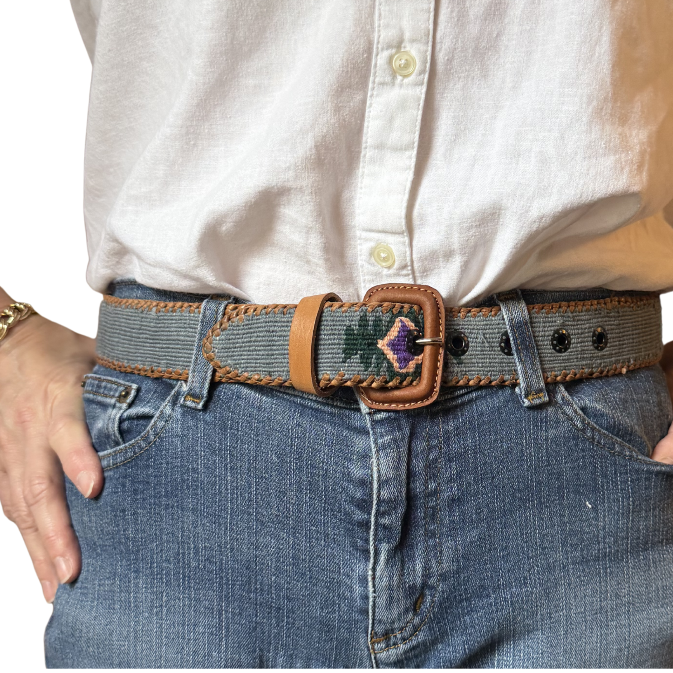 Person wearing a belt with a decorative buckle, white shirt, and blue jeans.