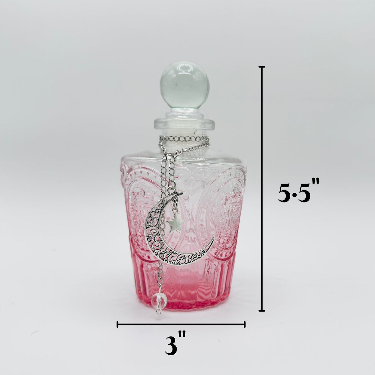 A clear glass perfume bottle with a pink gradient base, featuring a silver crescent moon pendant and a clear glass stopper. The image includes dimension lines indicating a height of 5.