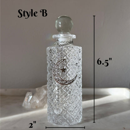 A clear textured glass bottle with a round stopper and a silver crescent moon and star pendant, shown with dimension labels reading 6.5 inches tall and 2 inches wide on a neutral background.