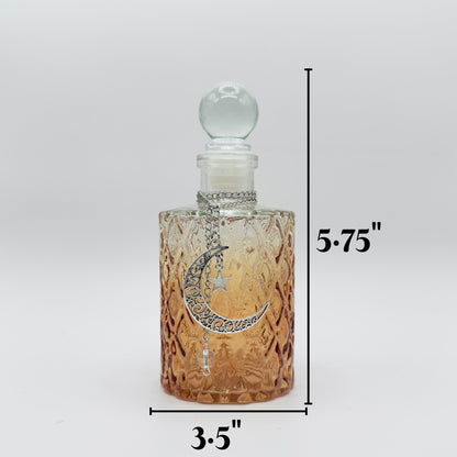 A clear glass perfume bottle with a textured amber-tinted body, a silver crescent moon and star pendant, and a clear glass stopper. Black dimension lines indicate a height of 5.