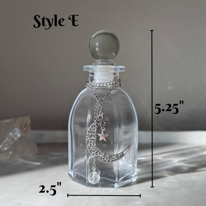 A clear glass perfume bottle with a silver crescent moon and star pendant necklace, shown with dimension lines indicating 5.25 inches tall and 2.