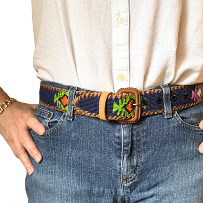 Person wearing a belt with an embroidered design on jeans and a white shirt.