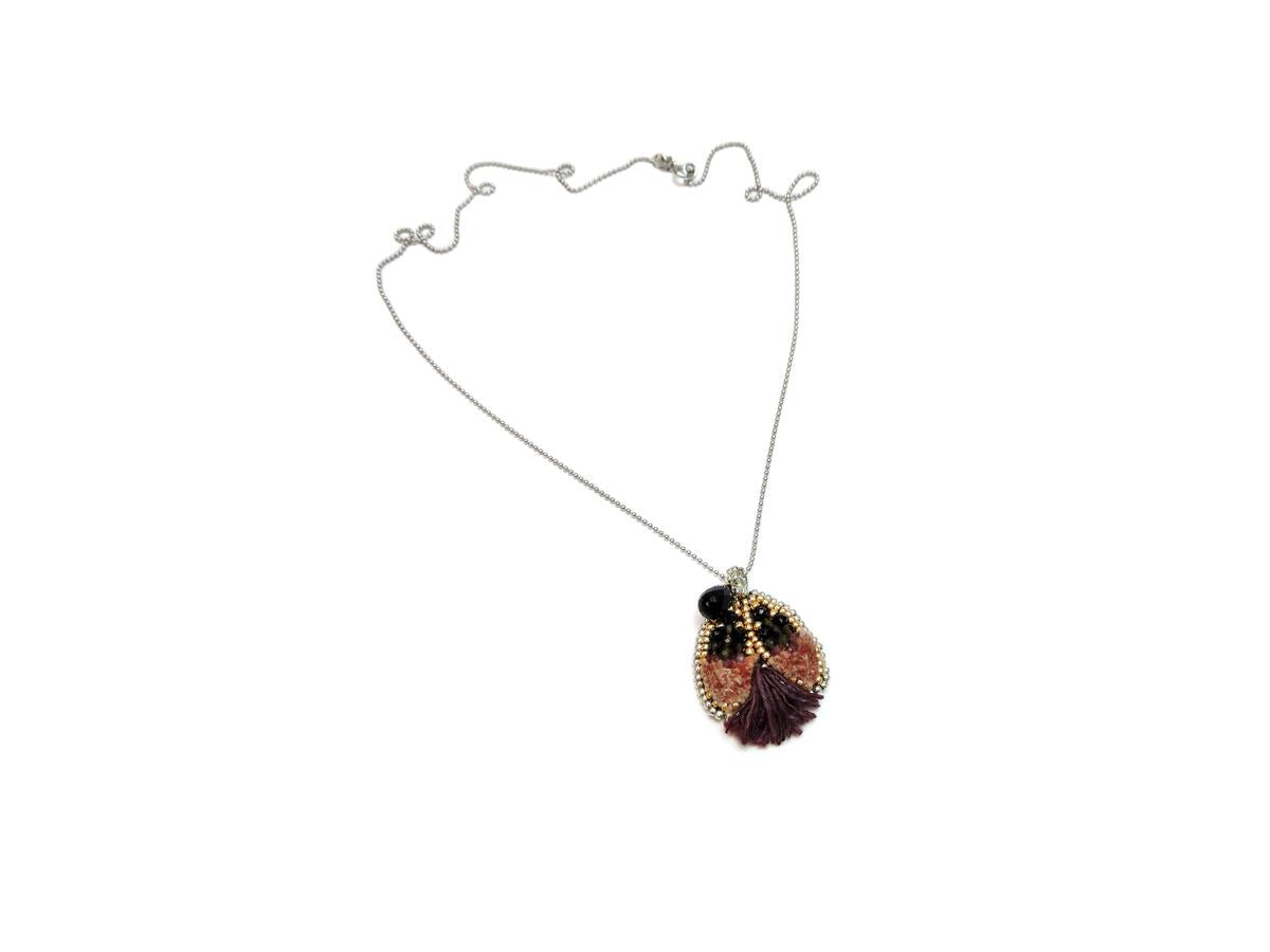 Ethically made, silver chain necklace with a ladybug pendant featuring purple and pink silk hand sewn on leather with ethically sourced bead stones and recycled materials, flay lay