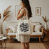 woman holding canvas tote bag that reads no human is illegal on stolen land in a retro script font