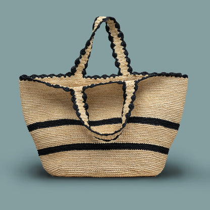 Artisan made raffia woven bag with black stripes and scallop trim on a solid background
