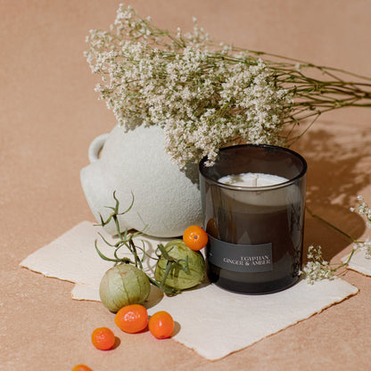 Candle with a white label, vase, and flowers on a beige surface