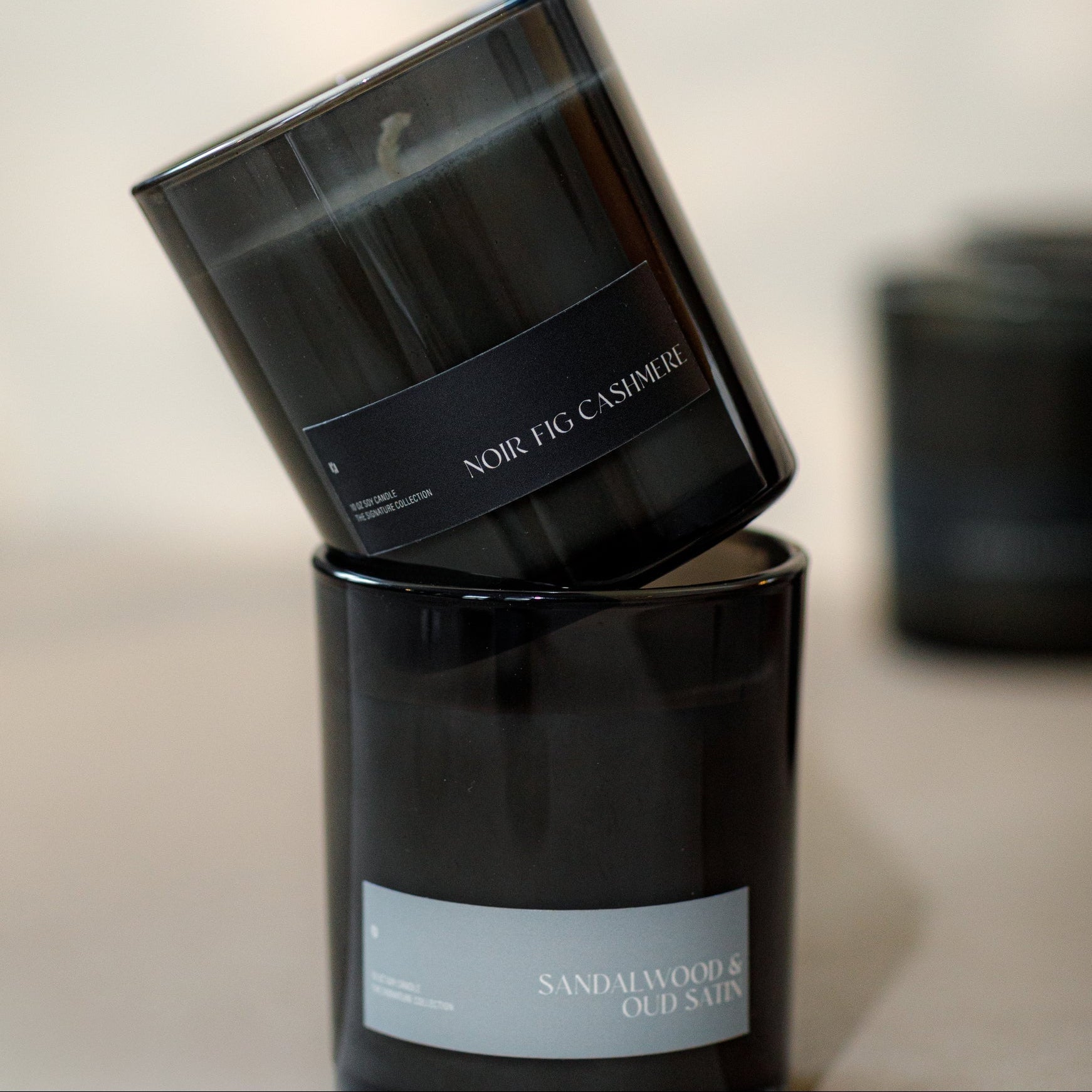 Two black candles stacked on a light surface with a blurred background