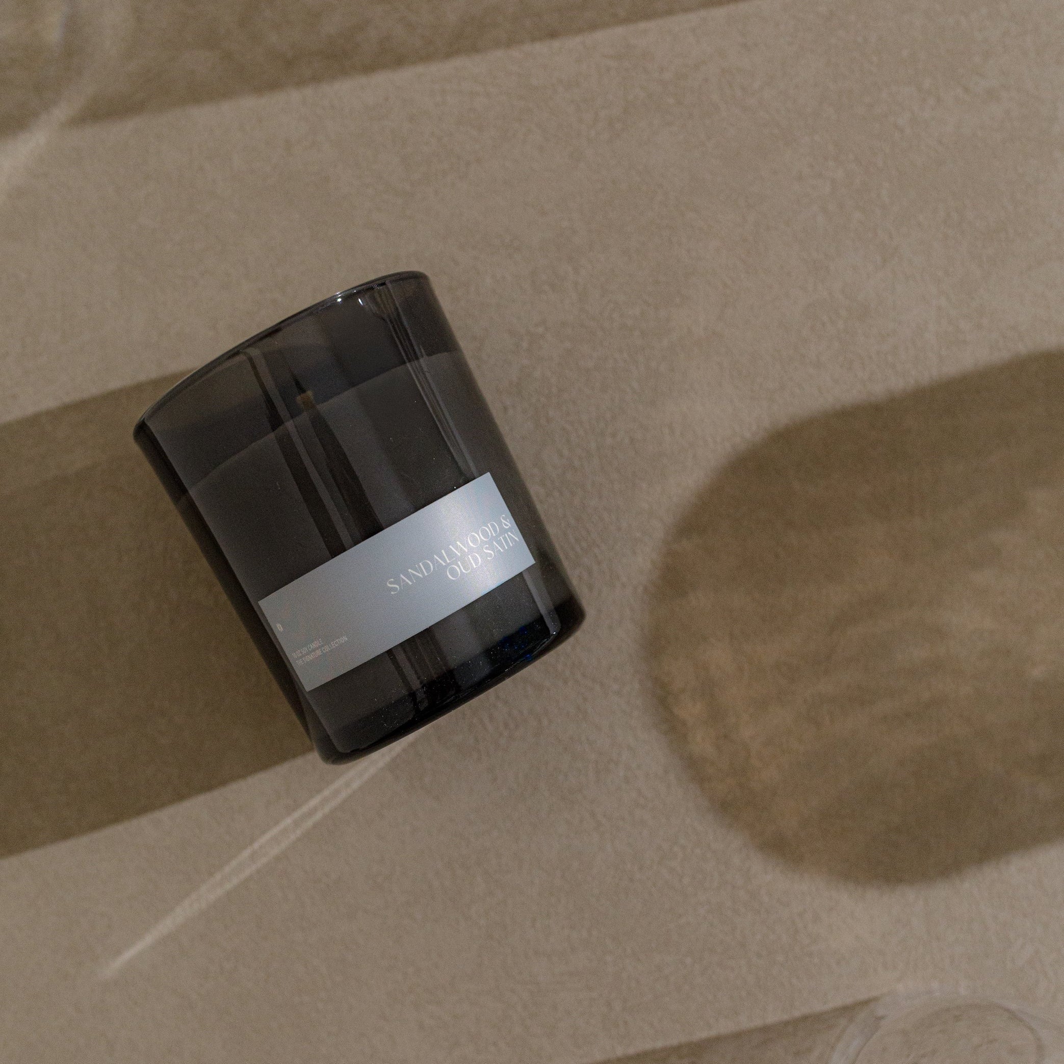 Black candle container with a white label on a beige surface