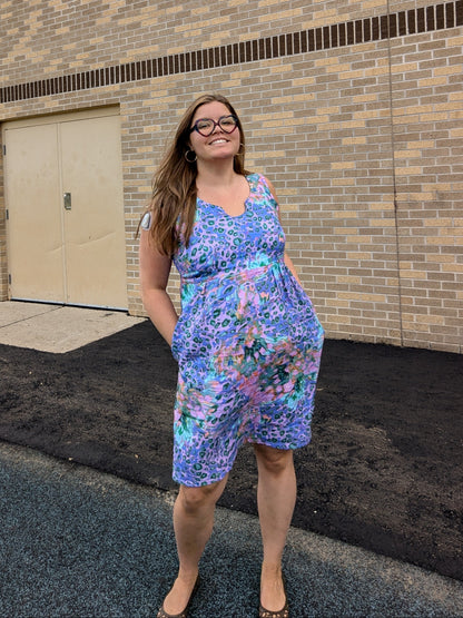 Woman in a floral trillium sun dress standing in front of a brick building