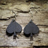 Pair of hand-painted black spade wooden dangle earrings featuring a bold playing card suit design displayed on rustic weathered wood