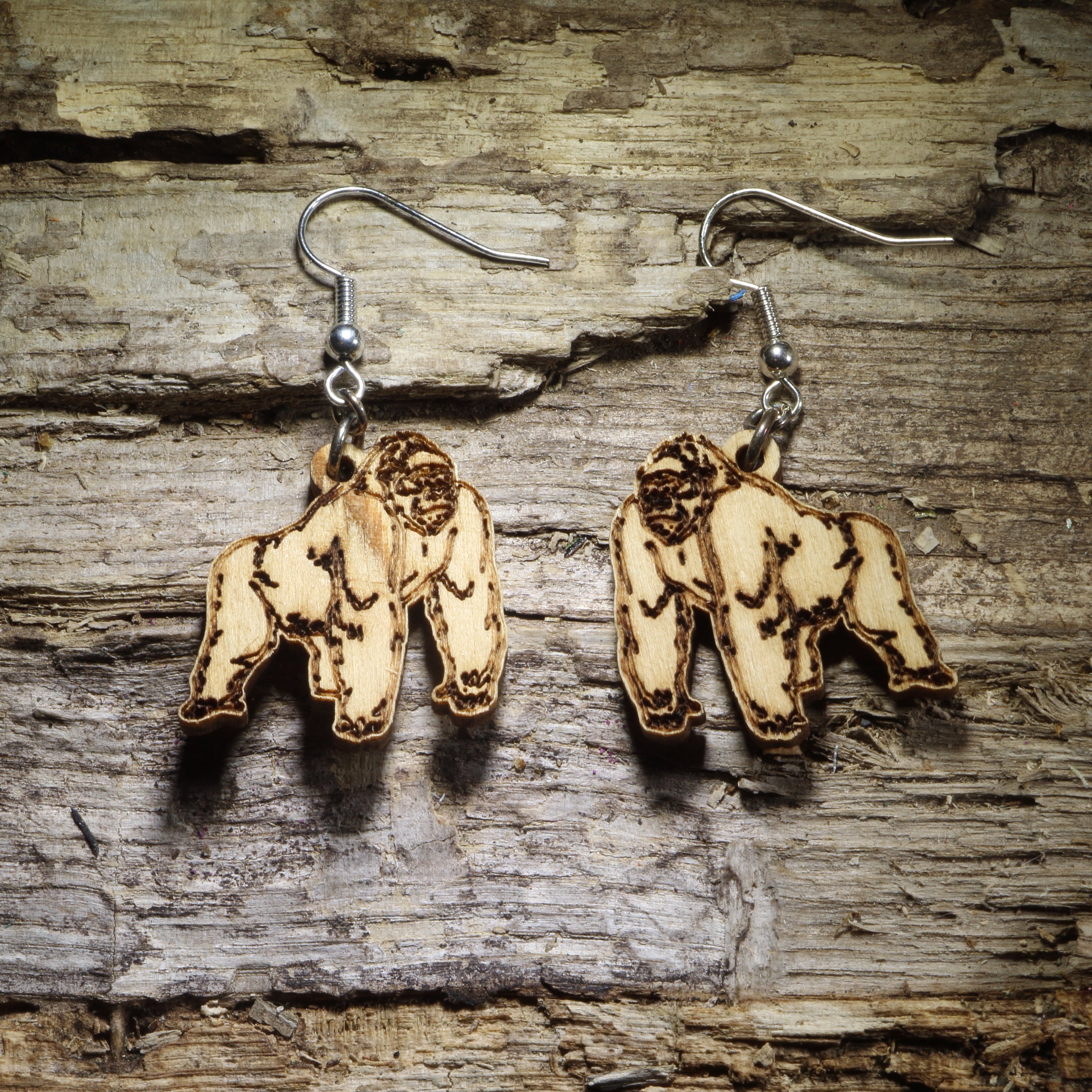 Pair of natural wood gorilla dangle earrings featuring detailed engraved gorilla designs displayed on rustic weathered wood