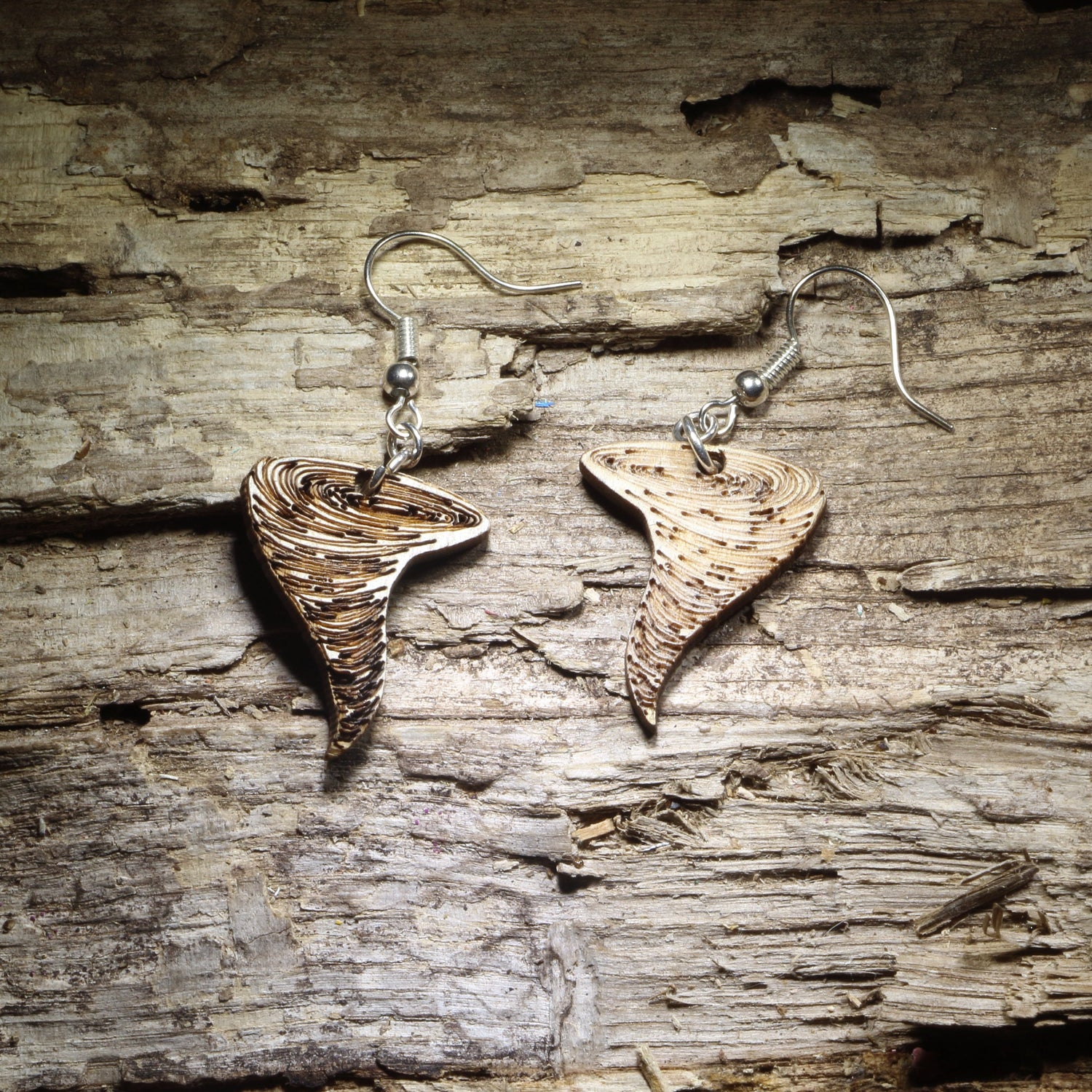 Pair of natural wood tornado dangle earrings with detailed swirling funnel cloud design displayed on rustic weathered wood