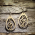 Pair of natural wood treble clef teardrop dangle earrings featuring an openwork musical note design displayed on rustic weathered wood