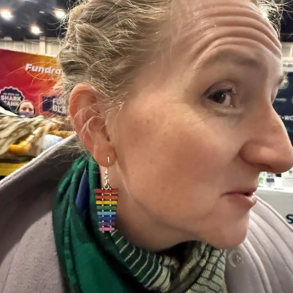 Person wearing hand-painted wooden rainbow xylophone dangle earrings on hypoallergenic .925 sterling silver hooks, showing the lightweight size and colorful music-inspired design when worn.