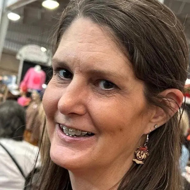 Person wearing hand-painted wooden scarecrow dangle earrings with smiling scarecrow faces, straw hair, and burgundy hats on hypoallergenic .925 sterling silver hooks, showing the lightweight size and fit when worn.