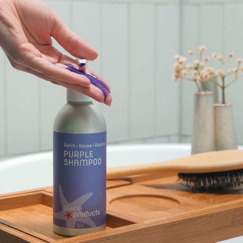 Eco Friendly Purple shampoo bring pumped into a hand with violet shampoo demonstrated for blonde, silver and gray hair. 
