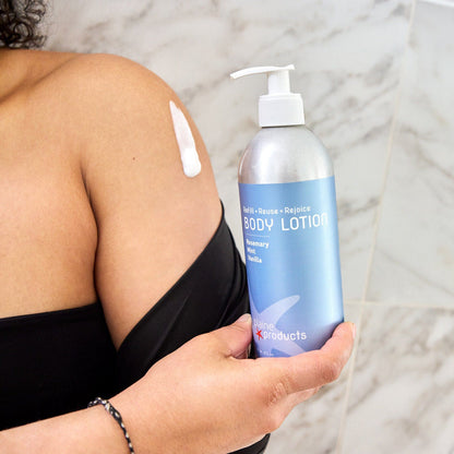Person holding a plastic free bottle of rosemary mint vanilla eco friendly body lotion and lotion on her skin with a marble background