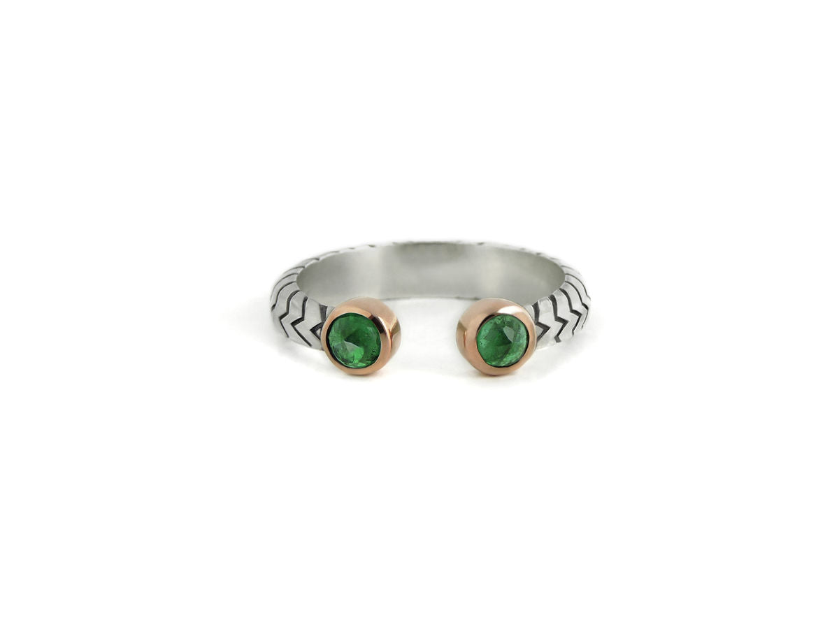 A split shank ring made of sterling silver with two 10k rose gold bezel set emeralds, made by hand with recycled metals and ethically sourced stones