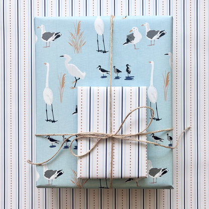 Two gift wrapped boxes, one with a light blue wrapping paper with white and grey birds, the other with a blue and white striped paper, tied with twine