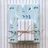 Two gift wrapped boxes, one with a light blue wrapping paper with white and grey birds, the other with a blue and white striped paper, tied with twine
