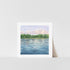 A framed art print depicting a landscape with a lake reflecting a blue sky, set against a white background.