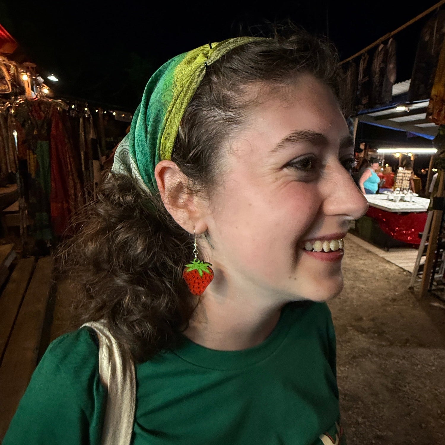 Side profile of a woman wearing hand-painted wooden strawberry dangle earrings featuring a vibrant red strawberry with green leaves. This lifestyle image demonstrates how these lightweight handmade wooden earrings with hypoallergenic .925 sterling silver hooks look when worn, making them ideal for summer festivals, berry lovers, casual outfits, and gift giving.