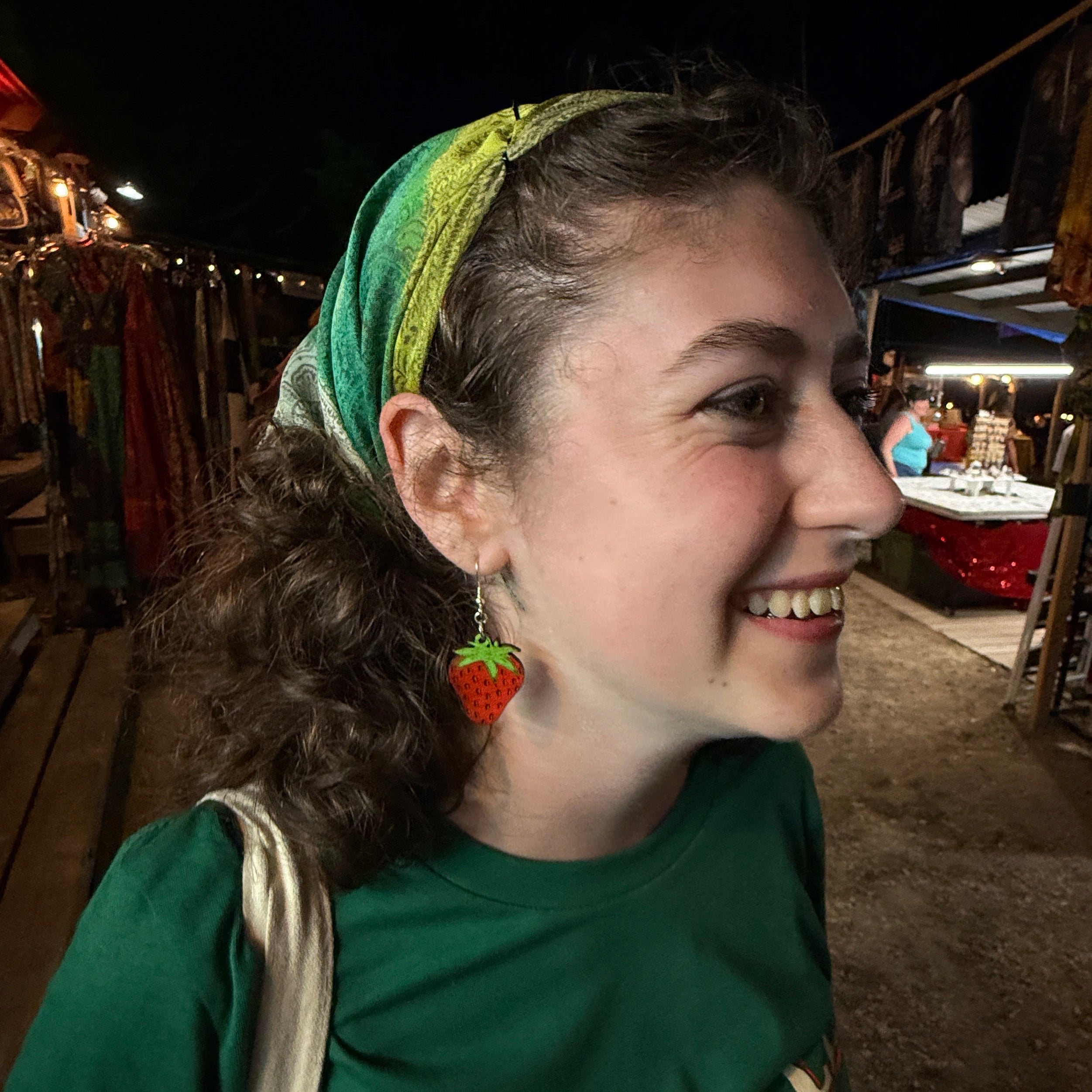 Side profile of a woman wearing hand-painted wooden strawberry dangle earrings featuring a vibrant red strawberry with green leaves. This lifestyle image demonstrates how these lightweight handmade wooden earrings with hypoallergenic .925 sterling silver hooks look when worn, making them ideal for summer festivals, berry lovers, casual outfits, and gift giving.