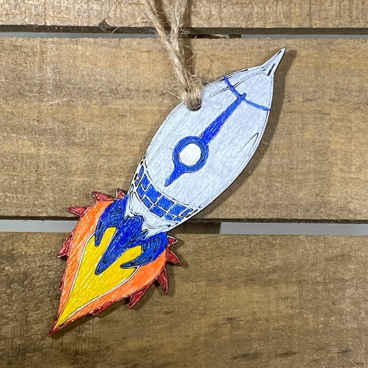 Hand-painted wooden silver rocket Christmas ornament featuring a sleek space-themed design with metallic finish and pointed nose cone, festive holiday decor for space enthusiasts and sci-fi lovers by Cate’s Concepts