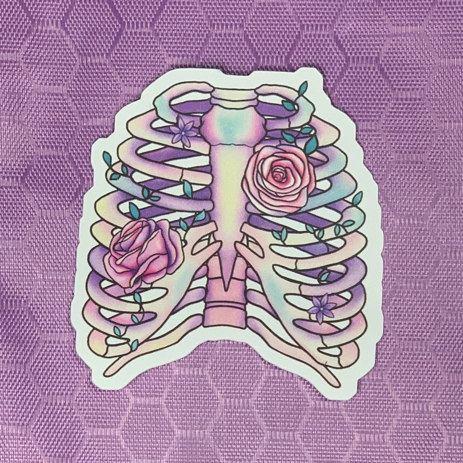 Our dreamy and whimsical die cut skeletal remains sticker features a softly pastel shaded ribcage with vined pink roses winding around the bones.&amp;nbsp;