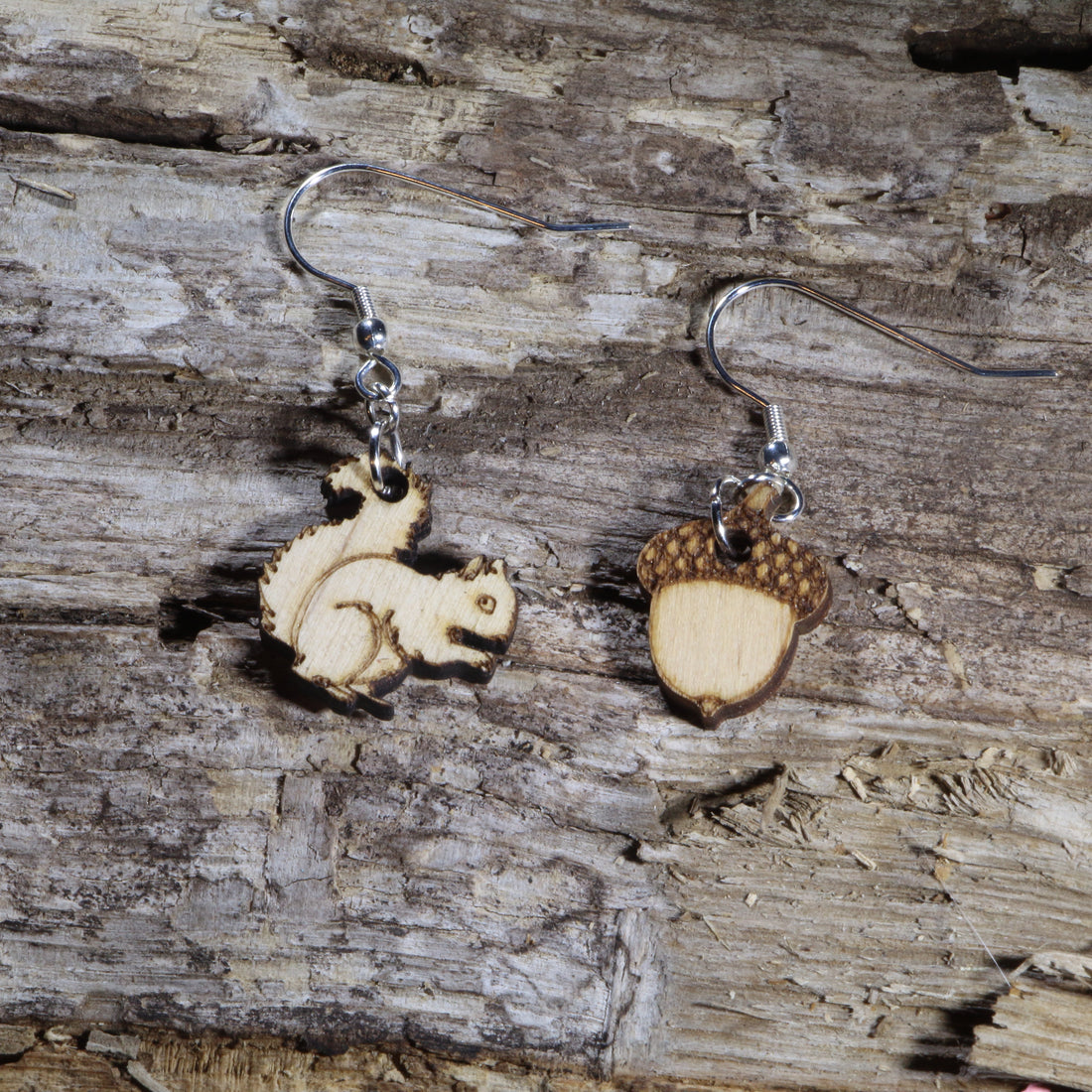 Handcrafted wooden mismatched squirrel and acorn dangle earrings featuring a playful woodland design with natural wood tones and engraved details. These lightweight earrings are finished with hypoallergenic .925 sterling silver hooks, making them a charming accessory for nature lovers, autumn outfits, and woodland-inspired style.