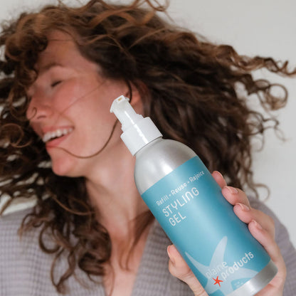 Curly haired woman holding an plastic free bottle of eco friendly styling gel 