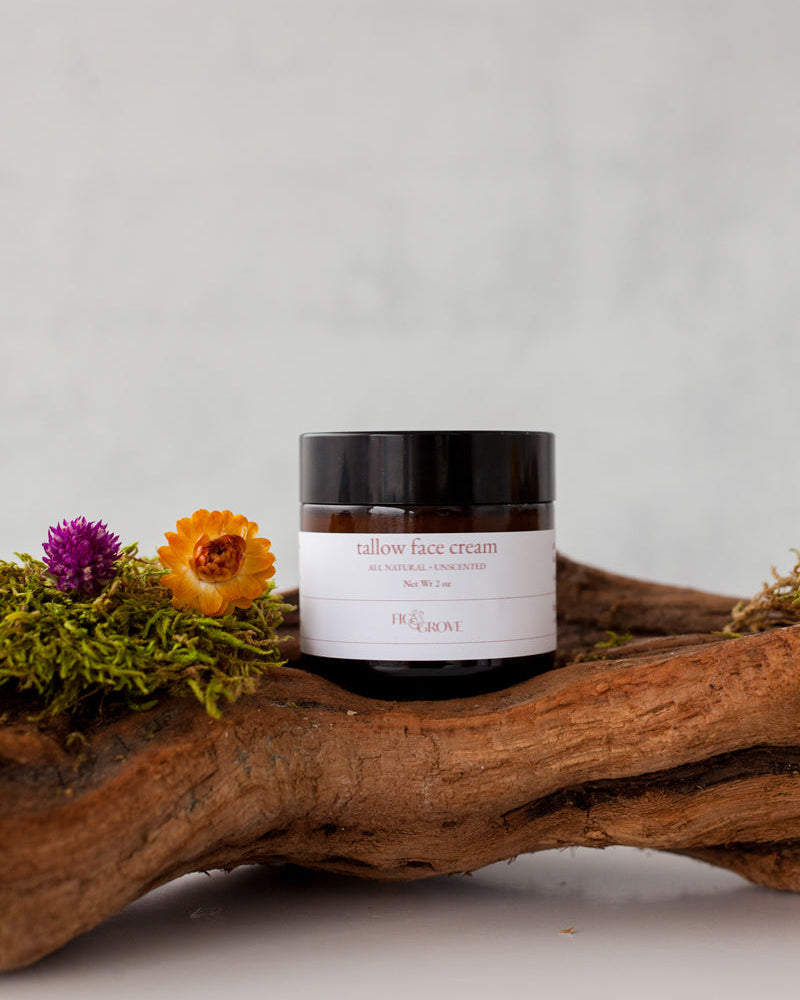 Jar of unscented regenerative suet tallow face cream for sensitive skin by Fig &amp; Grove on a wooden log with flowers against a light background
