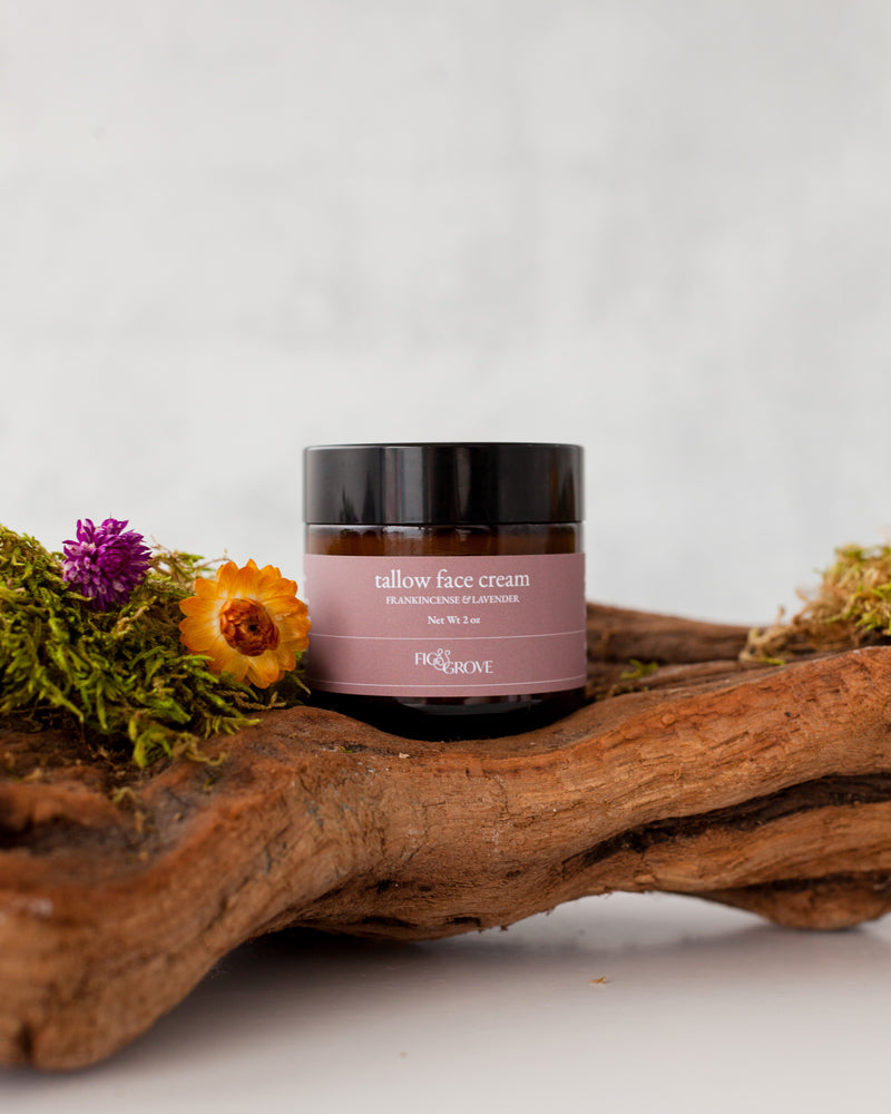 Jar of regenerative suet tallow face cream infused with yarrow &amp; calendula by Fig &amp; Grove on a wooden log with flowers and moss