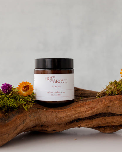 Jar of Fig &amp; Grove regenerative suet tallow body cream on a wooden log with flowers and moss.