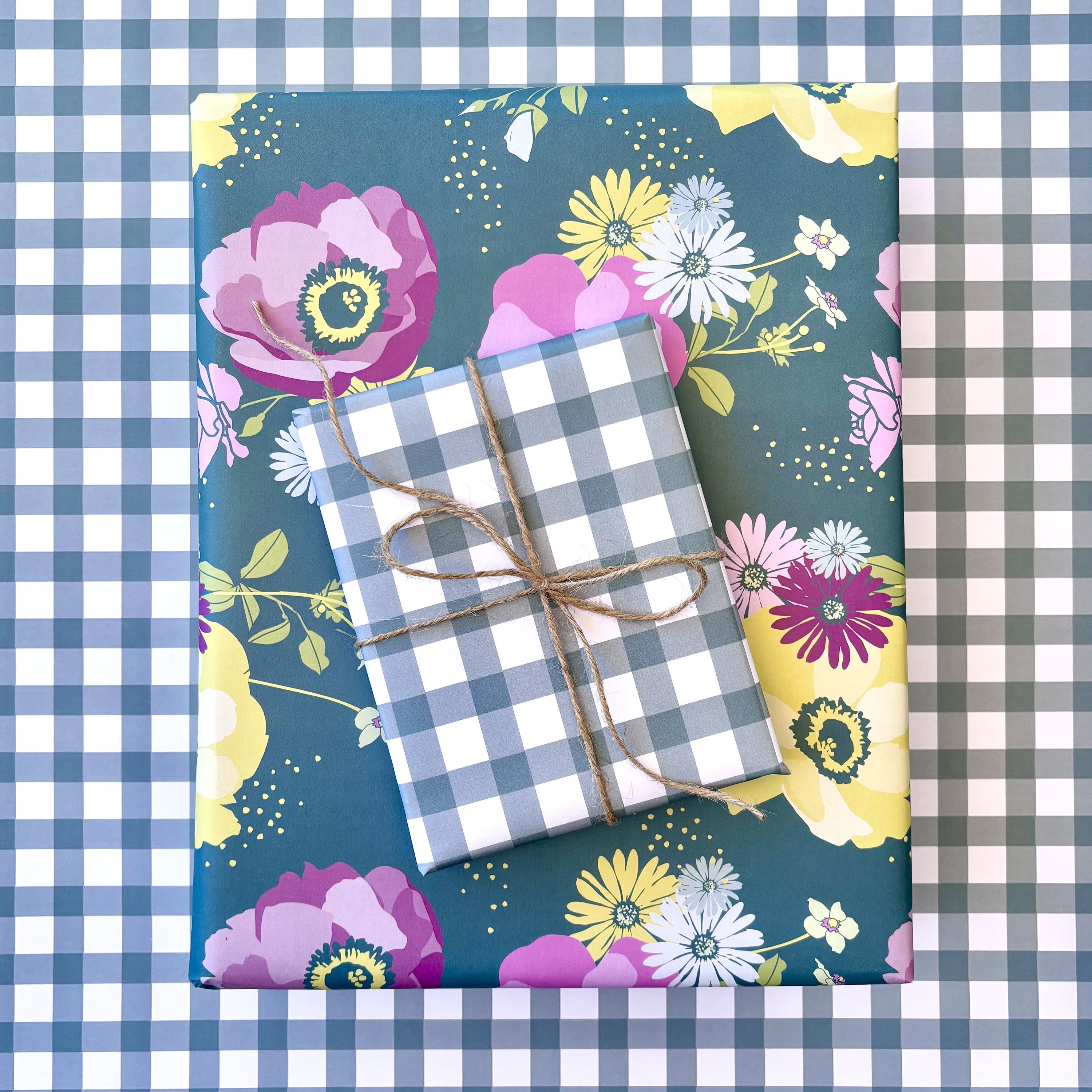 Floral-patterned paper with two wrapped gifts tied with twine on a gingham plaid background