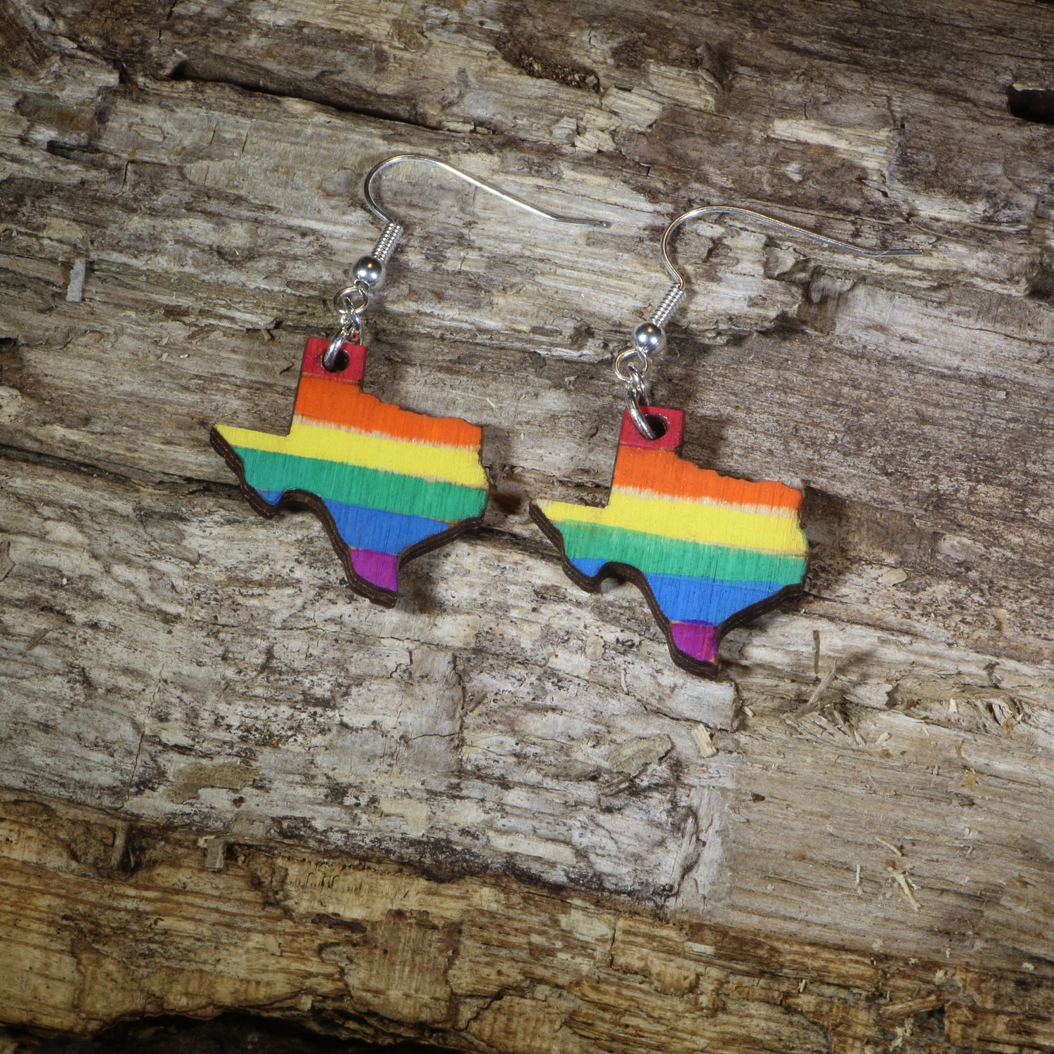Hand-painted wooden Texas LGBTQ Pride dangle earrings featuring the Texas state silhouette with vibrant rainbow pride stripes, hypoallergenic sterling silver hooks, and lightweight LGBTQ+ state pride jewelry by Cate&