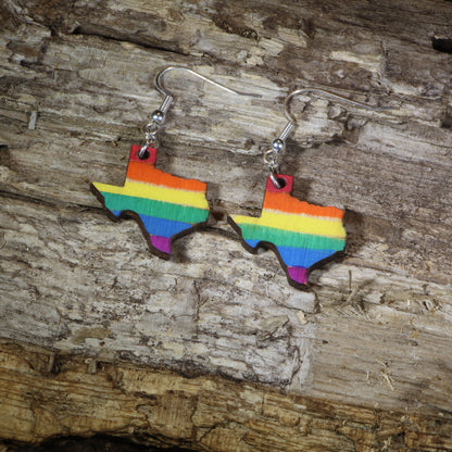 Hand-painted wooden Texas LGBTQ Pride dangle earrings featuring the Texas state silhouette with vibrant rainbow pride stripes, hypoallergenic sterling silver hooks, and lightweight LGBTQ+ state pride jewelry by Cate&