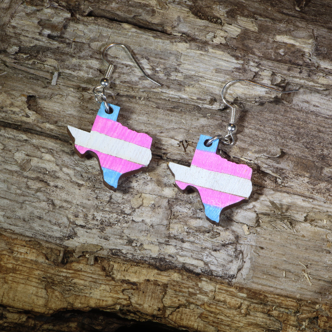 Hand-painted wooden Texas transgender pride dangle earrings featuring the Texas state silhouette with pink, blue, and white transgender pride stripes, hypoallergenic sterling silver hooks, and lightweight LGBTQ+ state pride jewelry by Cate&