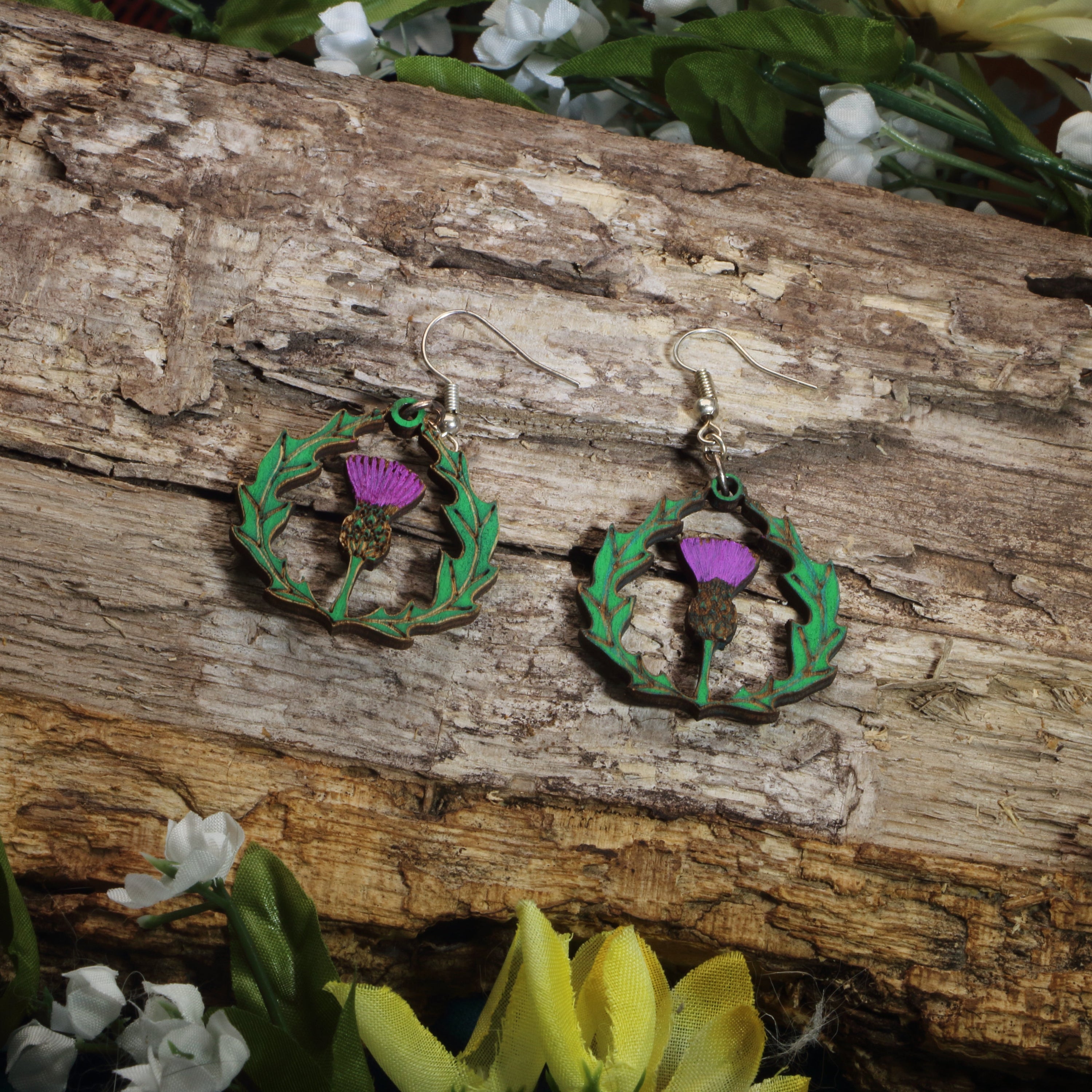 Hand-painted wooden thistle dangle earrings featuring a purple Scottish thistle framed by Celtic-inspired greenery, hypoallergenic sterling silver hooks, and lightweight heritage jewelry for Scottish pride, Celtic culture, and nature lovers by Cate’s Concepts