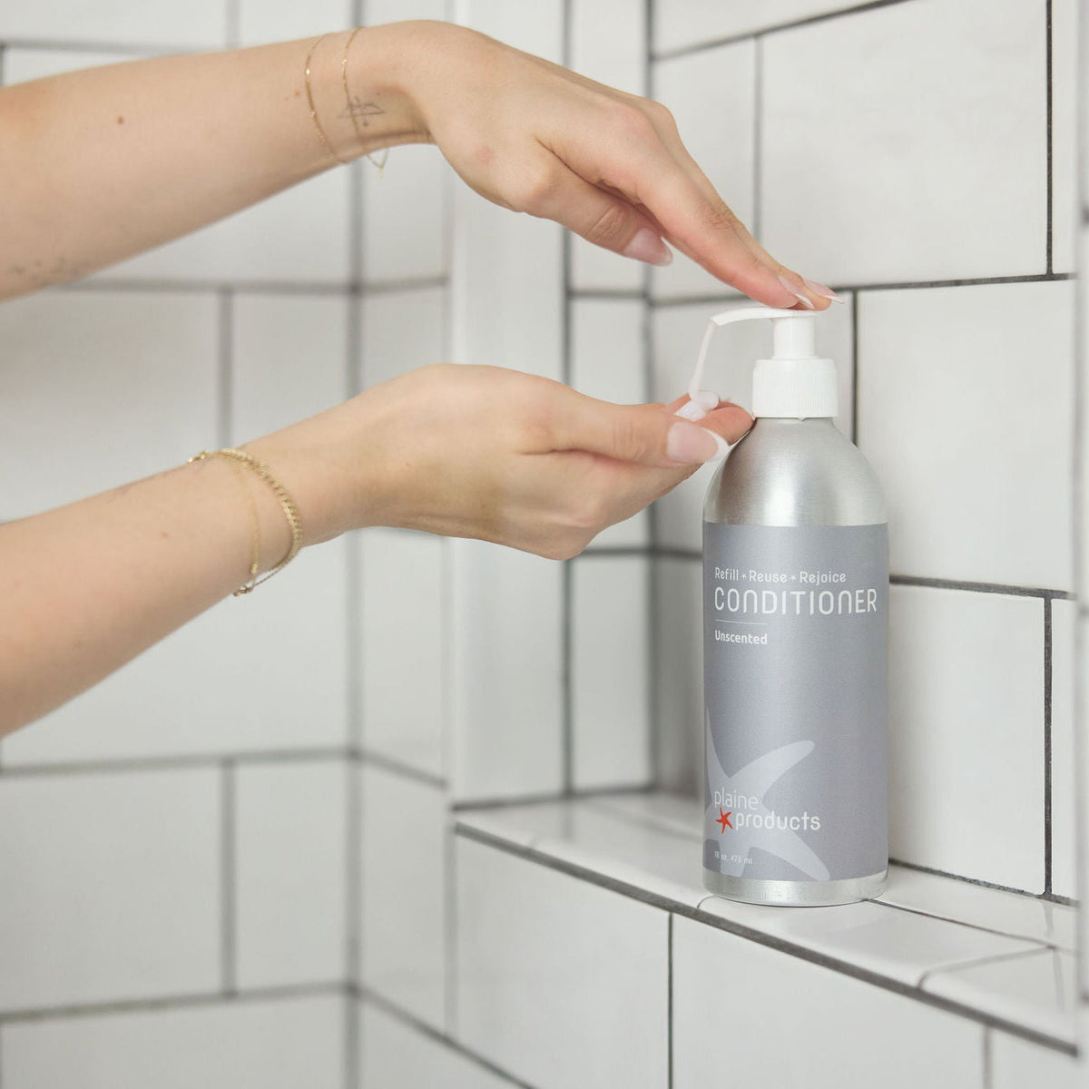 Unscented conditioner being pumped out of a plastic free bottles in shower. Cruelty-free, biodegradable, vegan, reusable, fragrance-free hair care in aluminum bottle